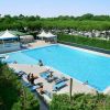 Piscina all'aperto con sdraio e persone che si rilassano, circondata da vegetazione.