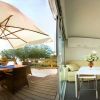 Area con terrazza in legno, ombrellone grande e tavolo, accanto a salotto moderno con divano beige.