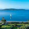 Vistoso paesaggio marino con barca a vela e spiaggia, circondato da verdi giardini.
