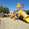 Parco giochi con scivolo giallo e seduta su ghiaia.