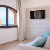 Soggiorno luminoso con divano beige, cuscini azzurri, finestra ad arco e TV a schermo piatto.