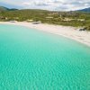 Spiaggia di sabbia bianca con mare turchese cristallino e colline sullo sfondo.