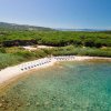 Spiaggia con lettini e ombrelloni, mare cristallino e vegetazione verdeggiante sullo sfondo.
