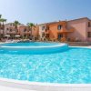 Grande piscina all’aperto contornata da edifici con terrazze e palme sullo sfondo.