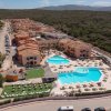 Vista aerea di un complesso turistico con piscine, edifici beige e area verde circostante.