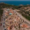 Complesso residenziale con tetti in tegole, vegetazione circostante e mare in lontananza.