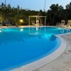 Piscina all'aperto illuminata di sera, circondata da lettini e vegetazione.