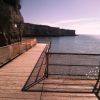 Passerella in legno su una costa rocciosa che si affaccia sul mare calmo e brillante.