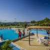 Una piscina all'aperto con bagnini e una zona relax con tavoli e sedie sotto un pergolato.