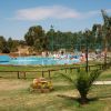 Una piscina all'aperto circondata da erba e alberi, con persone che si rilassano sui lettini.