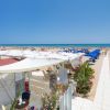 Spiaggia con ombrelloni blu e chiosco a sinistra.