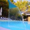 Cascata in piscina con lettini e alberi sullo sfondo.