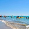 Spiaggia affollata, bagnanti in mare e vele colorate.