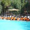 Persone in t-shirt arancioni sedute sul bordo di una piscina.