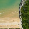 Spiaggia vista dall'alto con ombrelloni arancioni e mare.