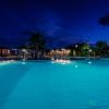 Piscina illuminata di notte con cielo scuro e alcune strutture sullo sfondo.