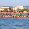 Una spiaggia affollata, con ombrelloni e lettini, e persone che nuotano nel mare.