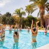 Persone fanno ginnastica in piscina sotto le palme.