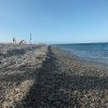 Spiaggia di ciottoli con mare e alcune sdraio distanti.