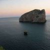 Scogliera solitaria al tramonto con mare calmo.