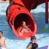 Bambini che giocano su uno scivolo d’acqua rosso in piscina.