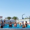 Persone che nuotano in piscina sotto il cielo azzurro.