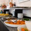 Buffet con piatti vari e ciotole bianche su un ripiano.