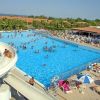 Grande piscina affollata con persone che nuotano e rilassano sotto ombrelloni.