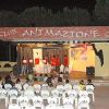 Spettacolo serale in un anfiteatro con sedie bianche e palco con tenda, scritto 