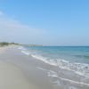 Spiaggia sabbiosa con onde leggere e cielo sereno.