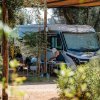 Camper parcheggiato tra gli alberi, persona seduta al tavolo.