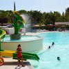 Scivolo giallo accanto a piscina, sole e spruzzi d'acqua.