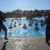 Persone partecipano a una lezione di acquagym in piscina con due istruttori in primo piano.