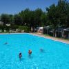 Una piscina con bambini che nuotano, circondata da alberi e sedie a sdraio.