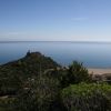 Vista panoramica di una collina verde che si affaccia su una vasta spiaggia e mare calmo.