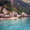 Acqua cristallina e scogliere rocciose con vegetazione lussureggiante sullo sfondo.