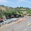 Spiaggia affollata con ombrelloni e colline verdi.