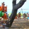 Parco giochi con scivolo colorato e bambini che giocano sotto un albero.