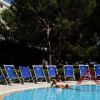 Una piscina con lettini blu, una persona in acqua e alberi sullo sfondo.