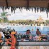 Un bar all'aperto vicino a una piscina, con persone che si godono bevande, palme sullo sfondo.