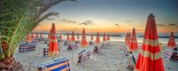 Spiaggia al tramonto con ombrelloni arancioni e righe blu.