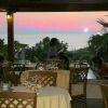 Ristorante all'aperto con tavoli apparecchiati, vista sul tramonto e mare.