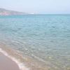 Una spiaggia con una distesa di sabbia dorata e mare calmo, montagne in lontananza.