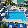 Piscina all'aperto con numerosi lettini e ombrelloni bianchi, circondata da strutture e verde.