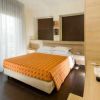 Camera d'albergo con letto matrimoniale e coperta arancione, arredamento moderno.