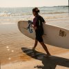 Persona con tavola da surf cammina verso il mare.