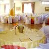 Sala da pranzo con tavoli rotondi apparecchiati e sedie coperte di bianco.
