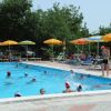Piscina affollata con persone che nuotano, circondata da ombrelloni gialli e arancioni.