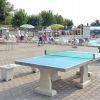 Area con tavoli da ping pong, ombrelloni e persone sedute.