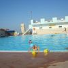 Una piscina all'aperto con bambini che giocano e un edificio sullo sfondo.